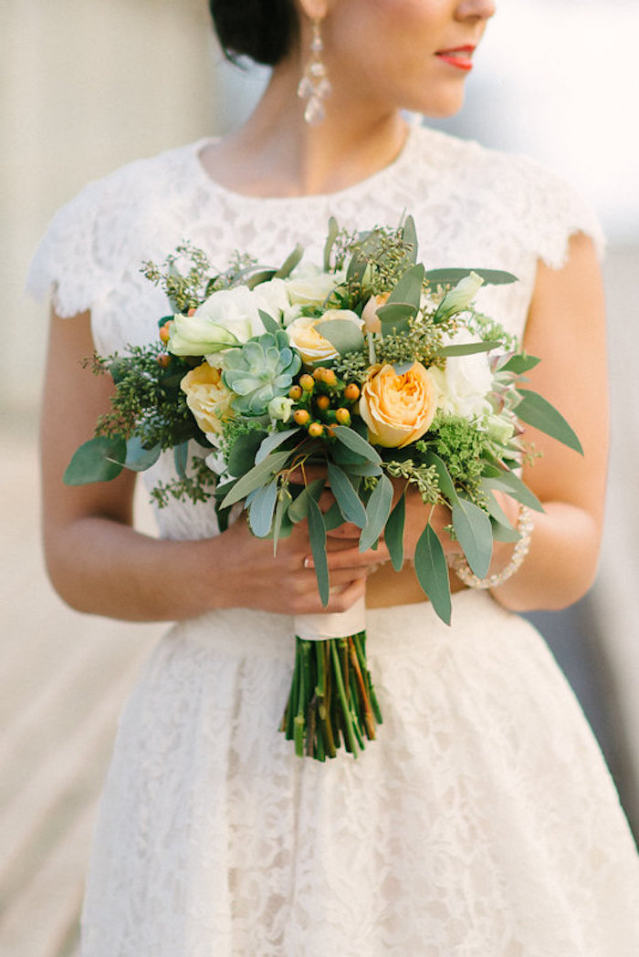 Bride in white dress holding Blooming yellow and white bouquet with green accents 