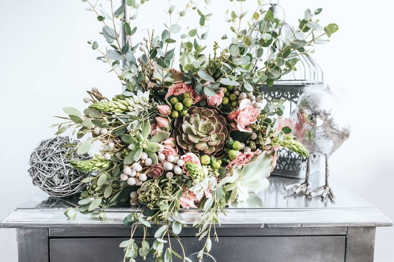 Green succulent floral arrangement with blush buds on mirrored table