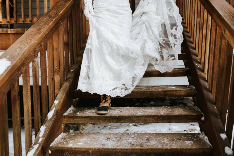 Bride in white lace skirt walks down icy wooden staircase in brown winter boots