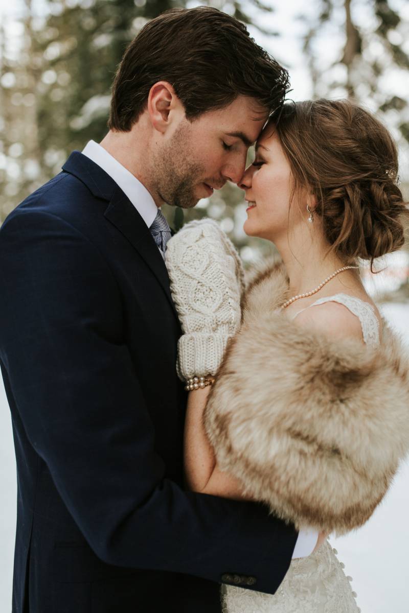 Groom embracing bride wearing white mittens and brown shawl 