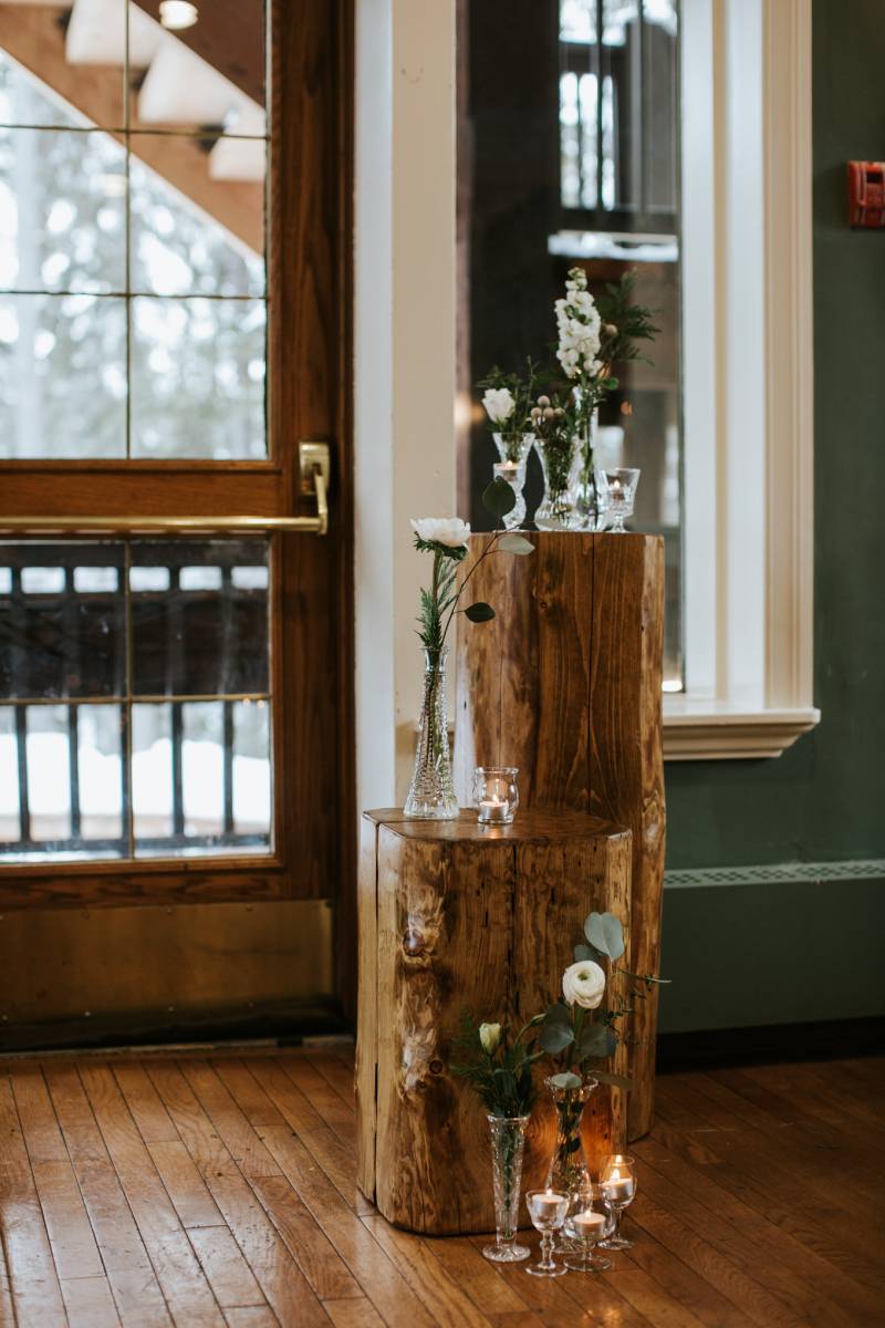 Two wooden stumps with white flowers in vases and candles on top