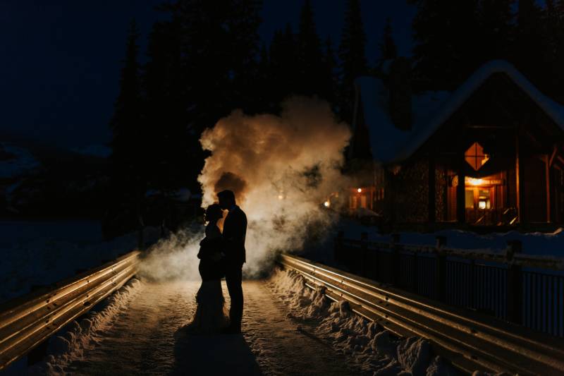 Bride and groom standing on dark metal bridge with smoke behind them