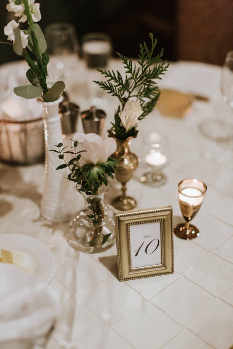 Place settings with white flowers in white and gold vases and candles