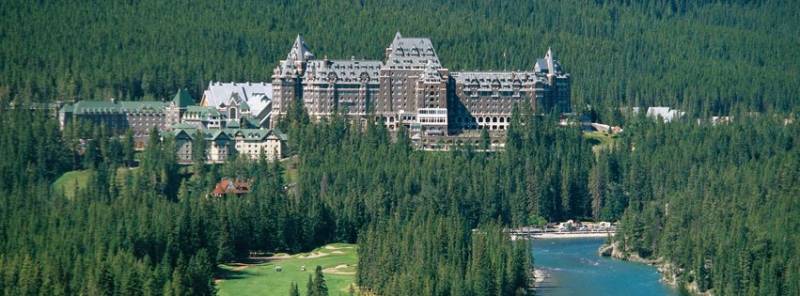 Fairmont Banff Springs Hotel surrounded by dense green forest and blue river
