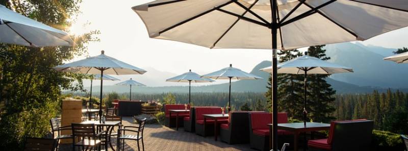 Outdoor patio with white umbrellas and red couches looking towards dense green forest and mountains 