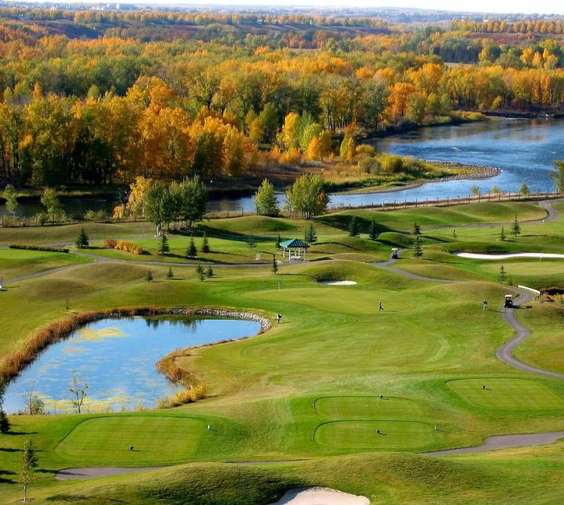 Overhead of golf course with small body of water and river with yellow and green fall leaves behind 