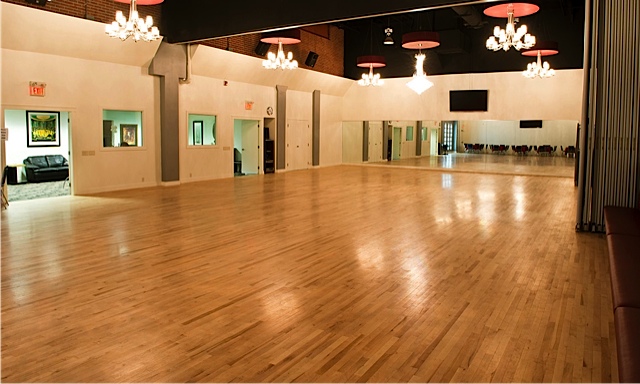 Large empty room with mirrors on wall and hanging chandeliers over light brown wood floor