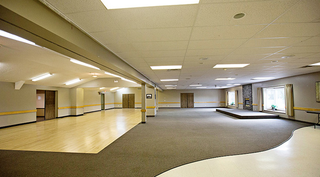 Large empty room with wavy carpeted floor and wooden floor areas 
