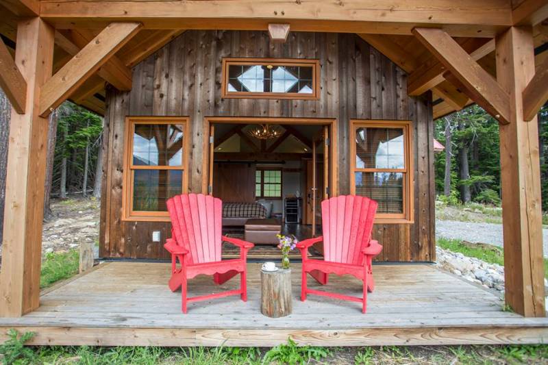 Two red armchairs sitting on wooden porch of small wood cabin in dense forest