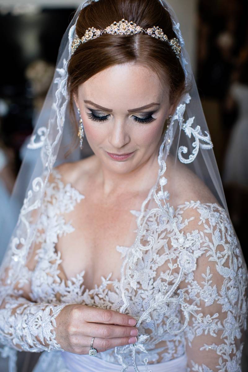 Bride in white lace dress and white veil looks down 
