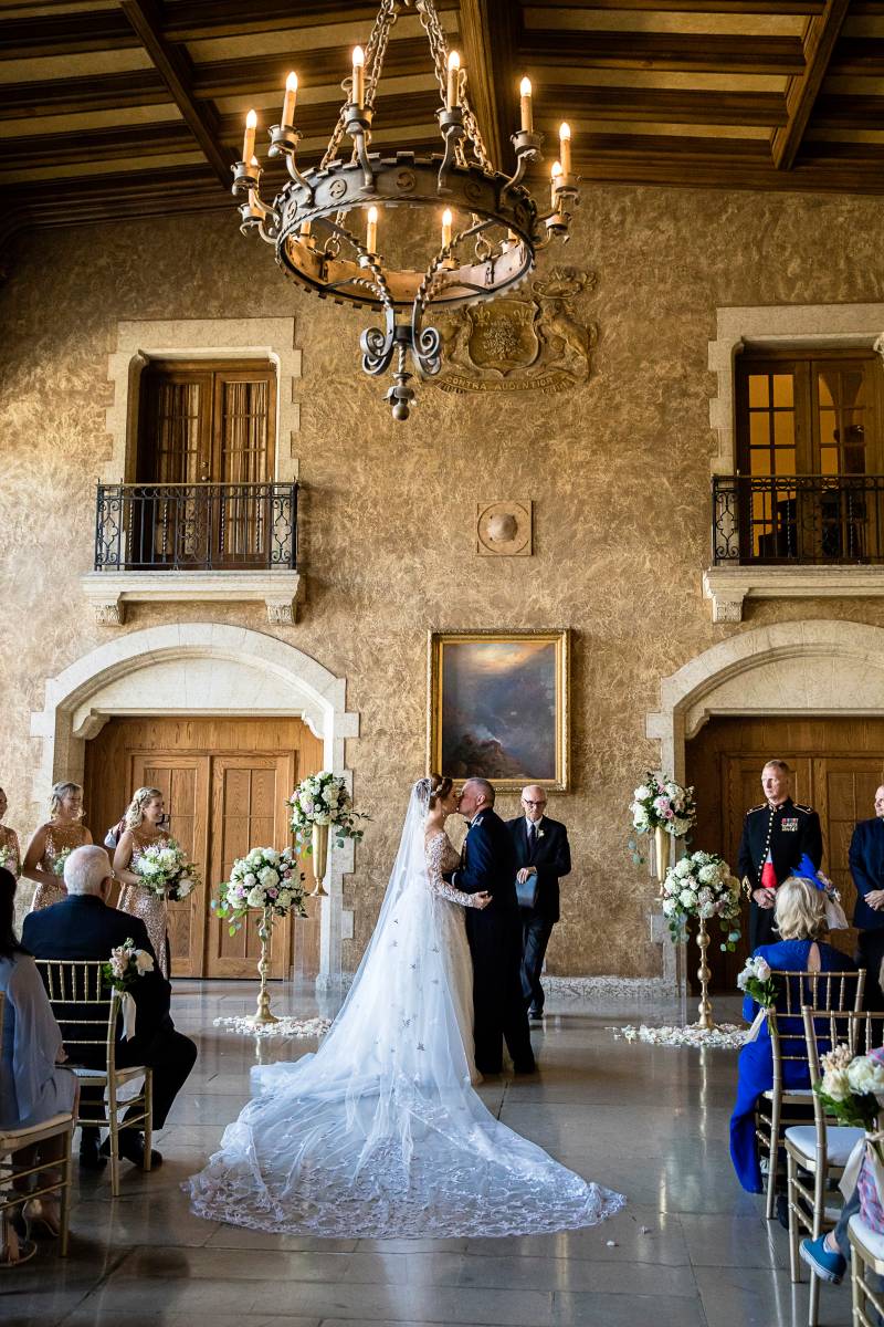 Bride and groom kiss while guests watch under chandelier 