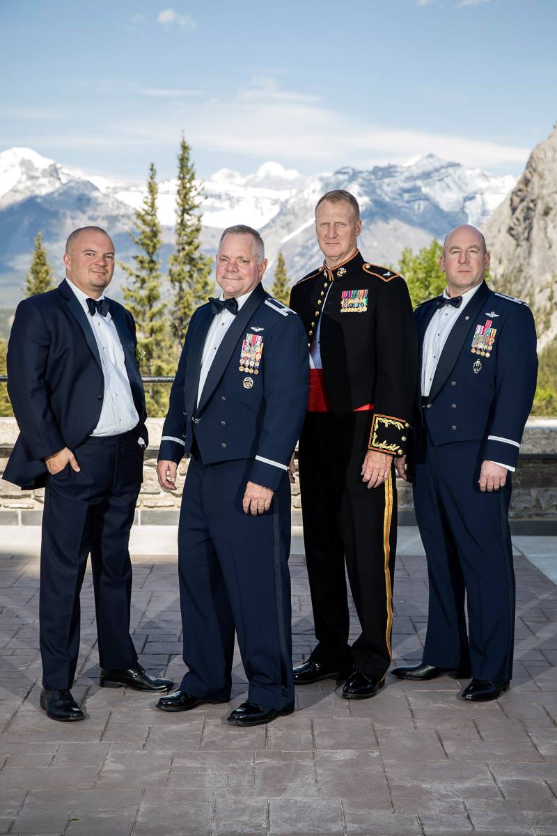 Groom and  groomsmen stand in uniform backing rocky mountains 