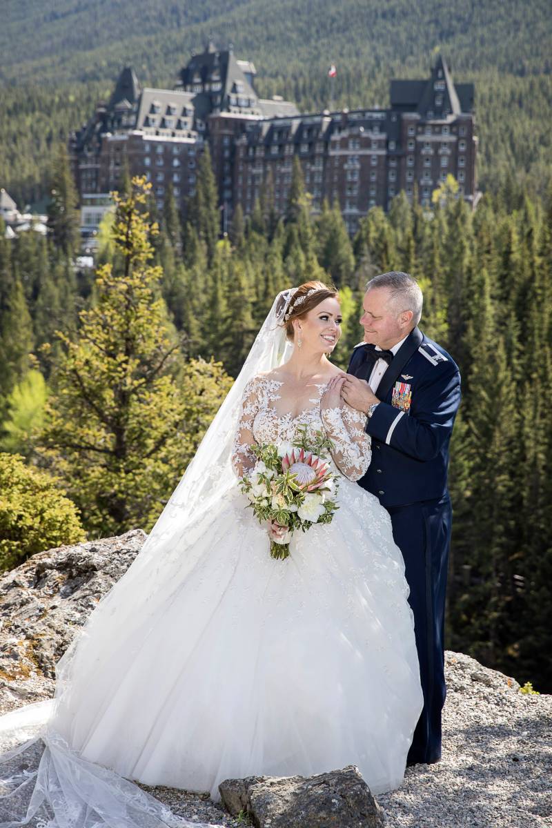 Bride and groom stand together smiling on rock facing banff springs hotel 