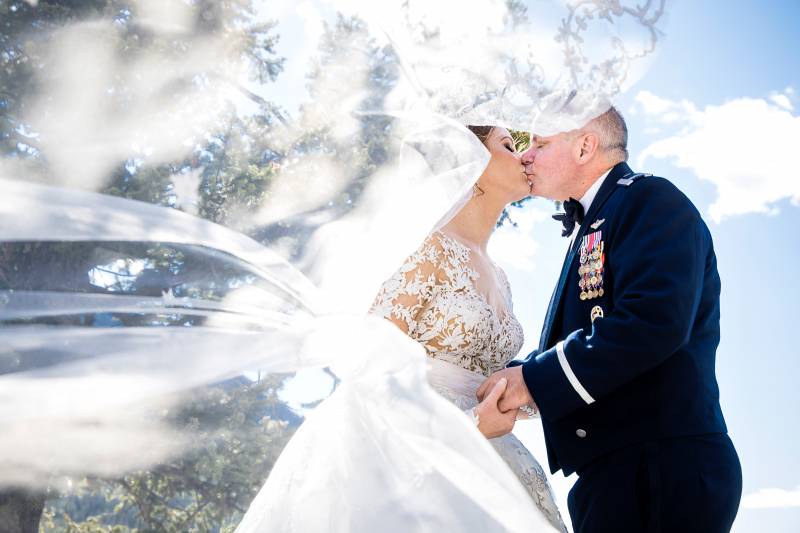 Bride and groom kiss while white veil flows in front 