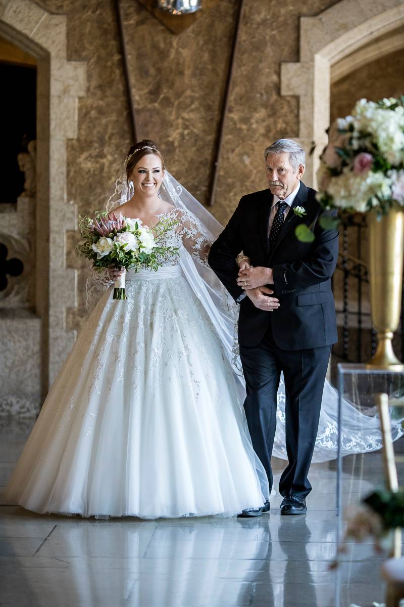 Bride in white dress walks in arms with man in black suit down aisle 
