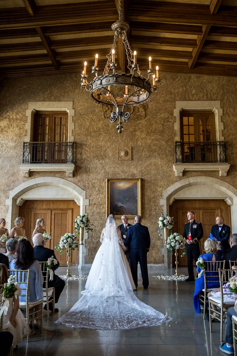 Bride and groom stand facing officiant under chandelier 