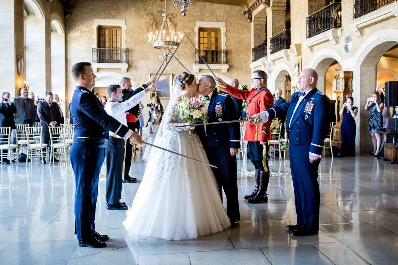 Men with swords stand at sides making archway while bride and groom kiss 