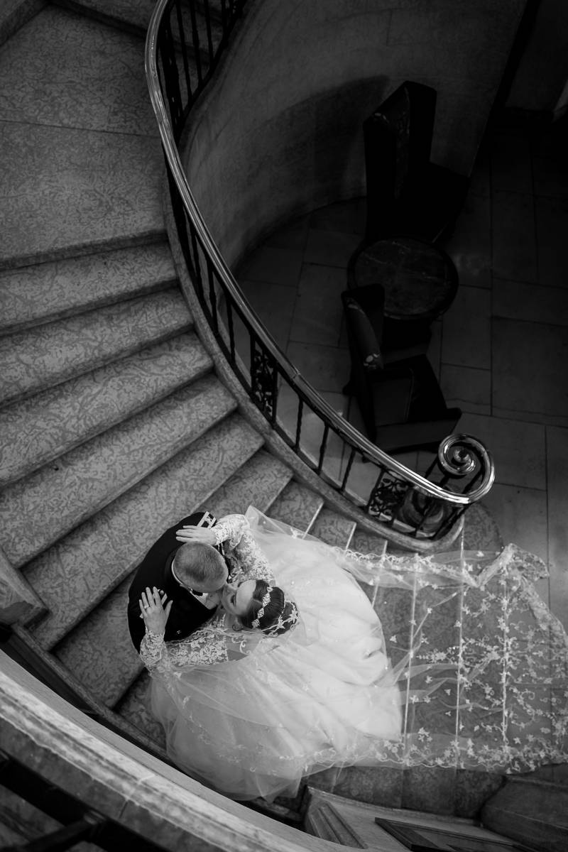 Bride and groom kiss at bottom of spiral staircase black and white 