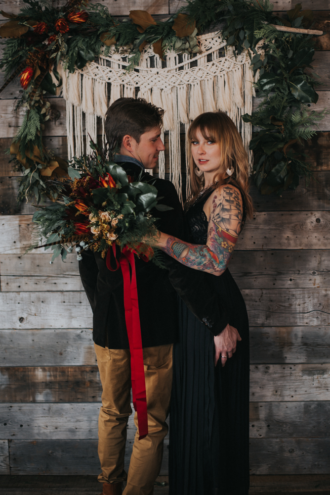 Man looks over shoulder at woman holding rust bouquet with red ribbon 