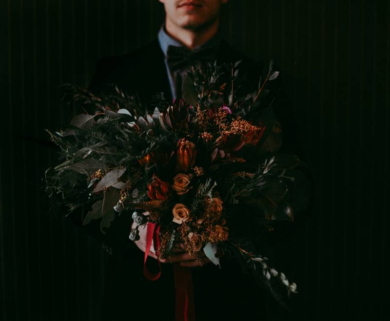 Man holds out crimson rust bouquet with red ribbon