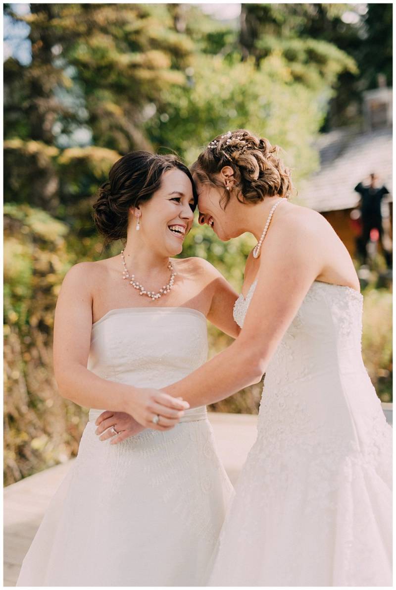 Brides laughing and smiling and embracing in shoulder-less white dresses