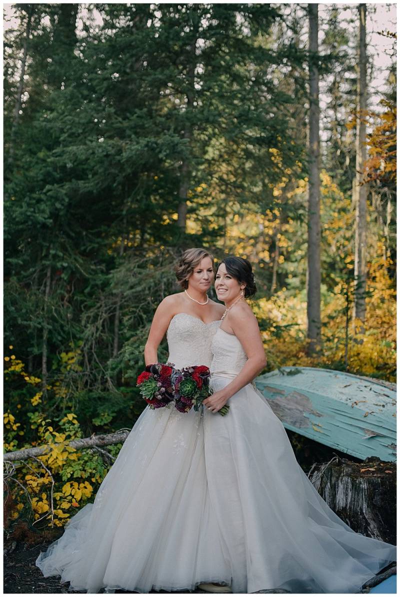 Brides embracing holding red and green bouquets on fall forest background