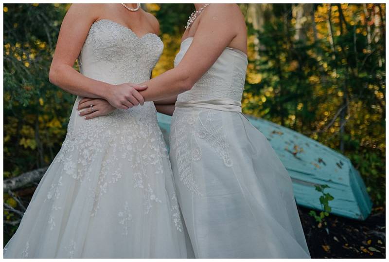 Brides embracing in white lace bodice dresses with lace skirts on fall backdrop