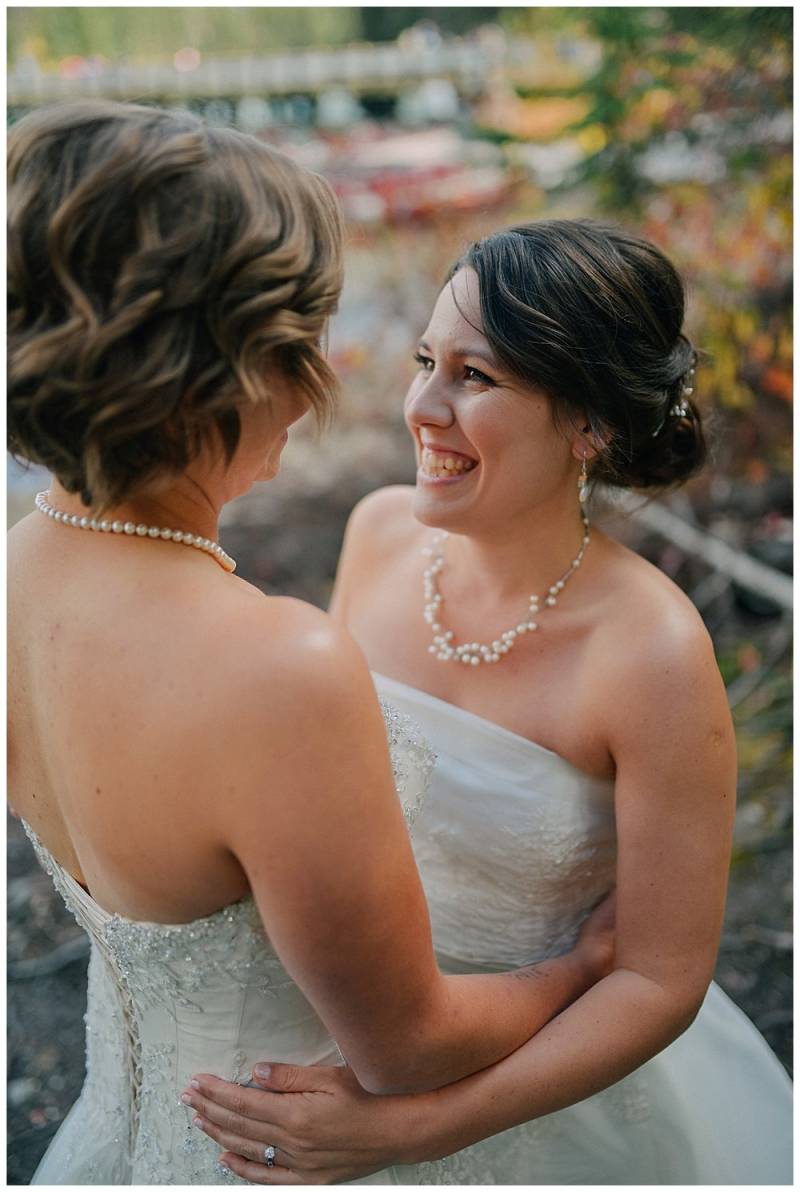 Brides in white lace bodice dresses smiling and embracing with peal necklaces