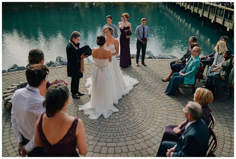 Wedding ceremony with brides wearing white dresses at the edge of lake 
