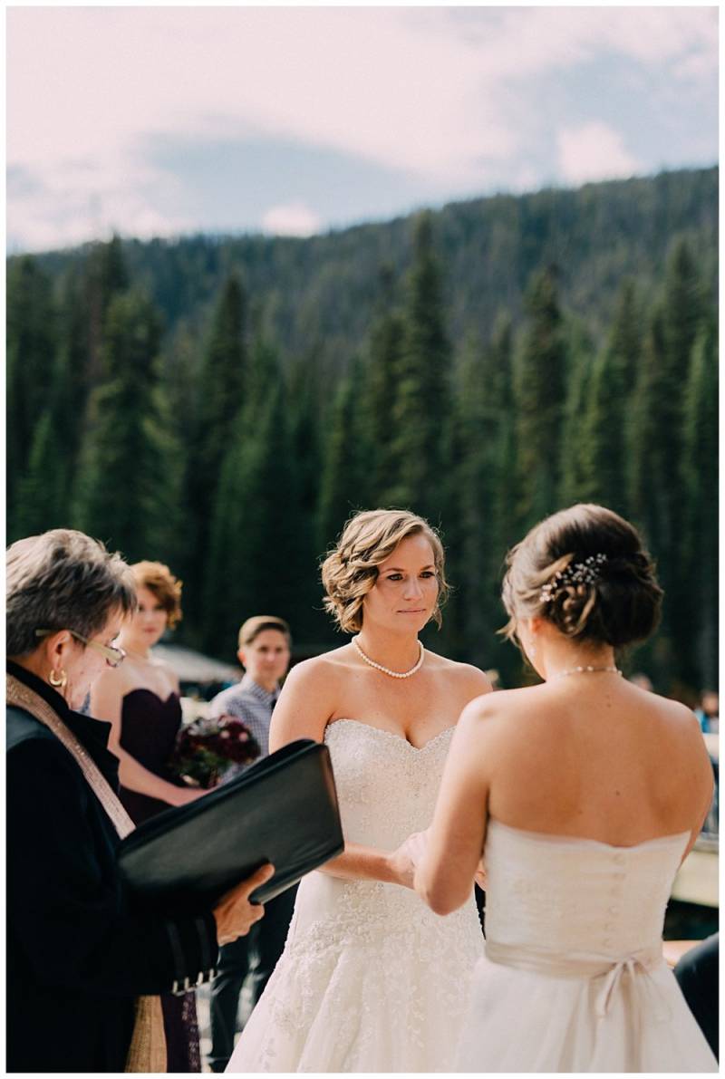 Brides holding hands as officiant reads vows on background of forest