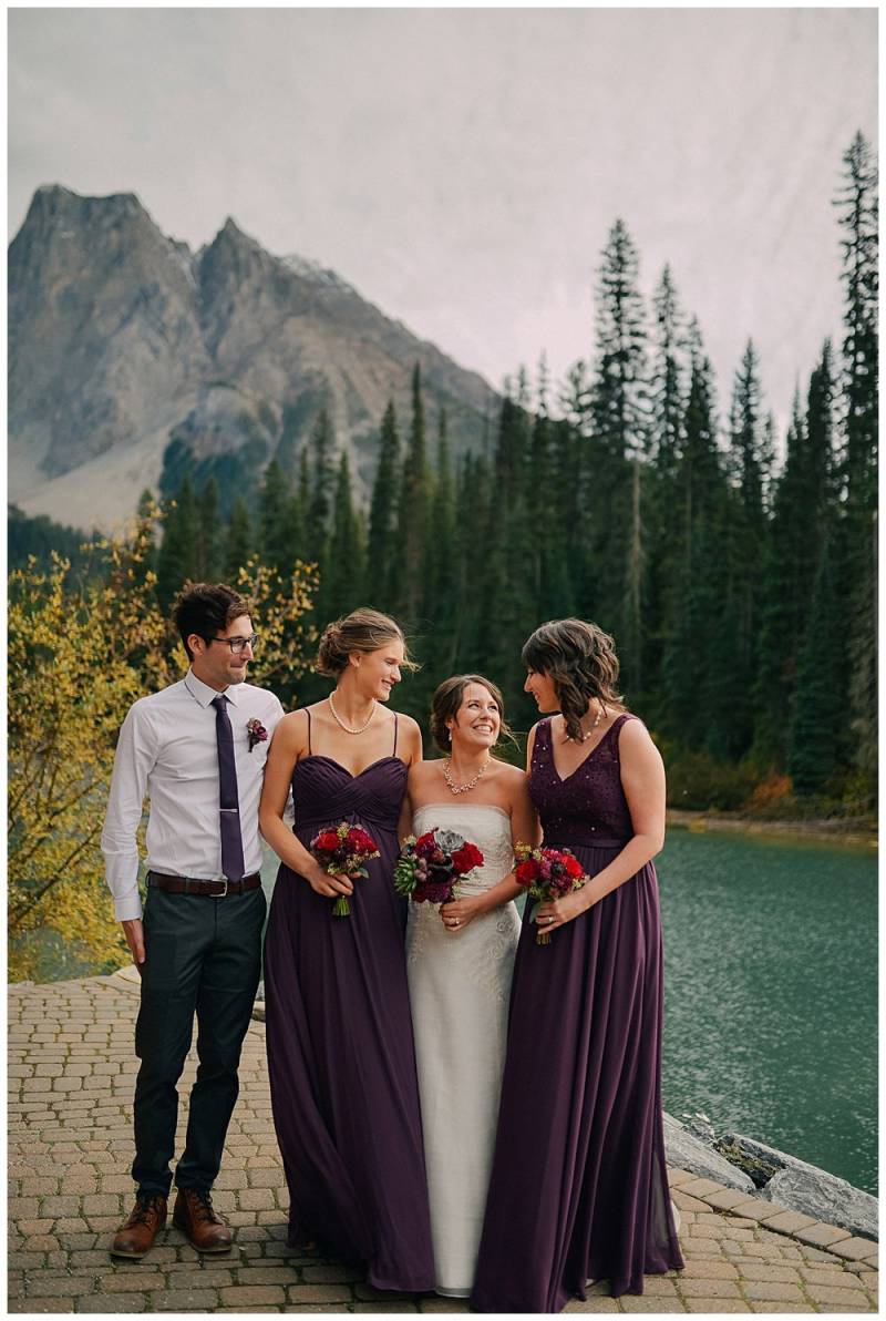 Bride and bridesmaids and groomsmen stand smiling at edge of water
