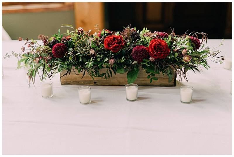 Rustic wood flower box centrepiece with red and pink and purple flowers on white table  