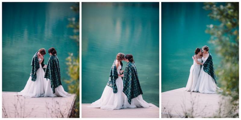 Brides in plaid green shawls and white dresses embracing by blue lake