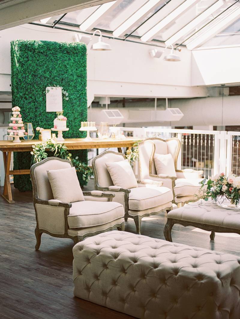 Dark wood and cream cushion seats in front of table with cakes and greenery wall