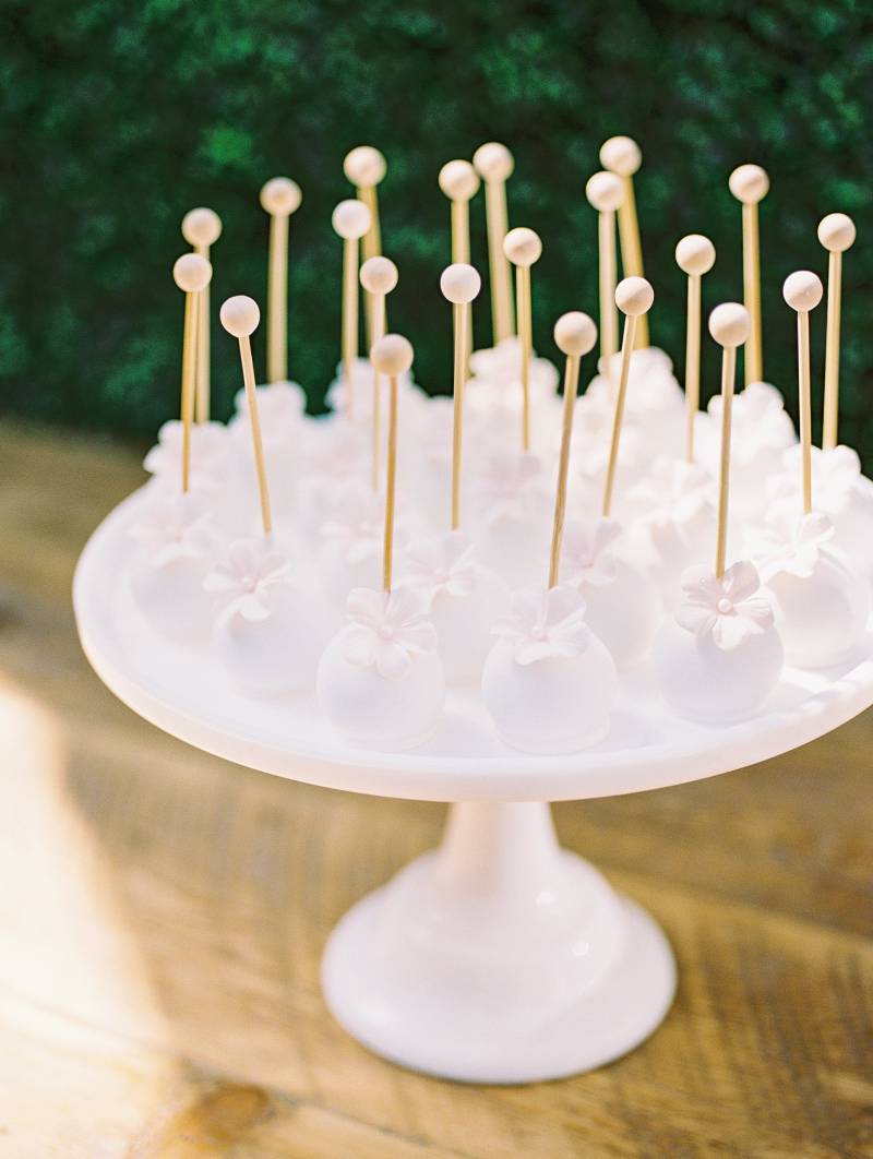White cake pops with wooden sticks on white cake display