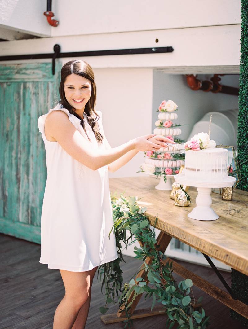 Woman in white shoulder less dress poses while pretending to cut cake on table