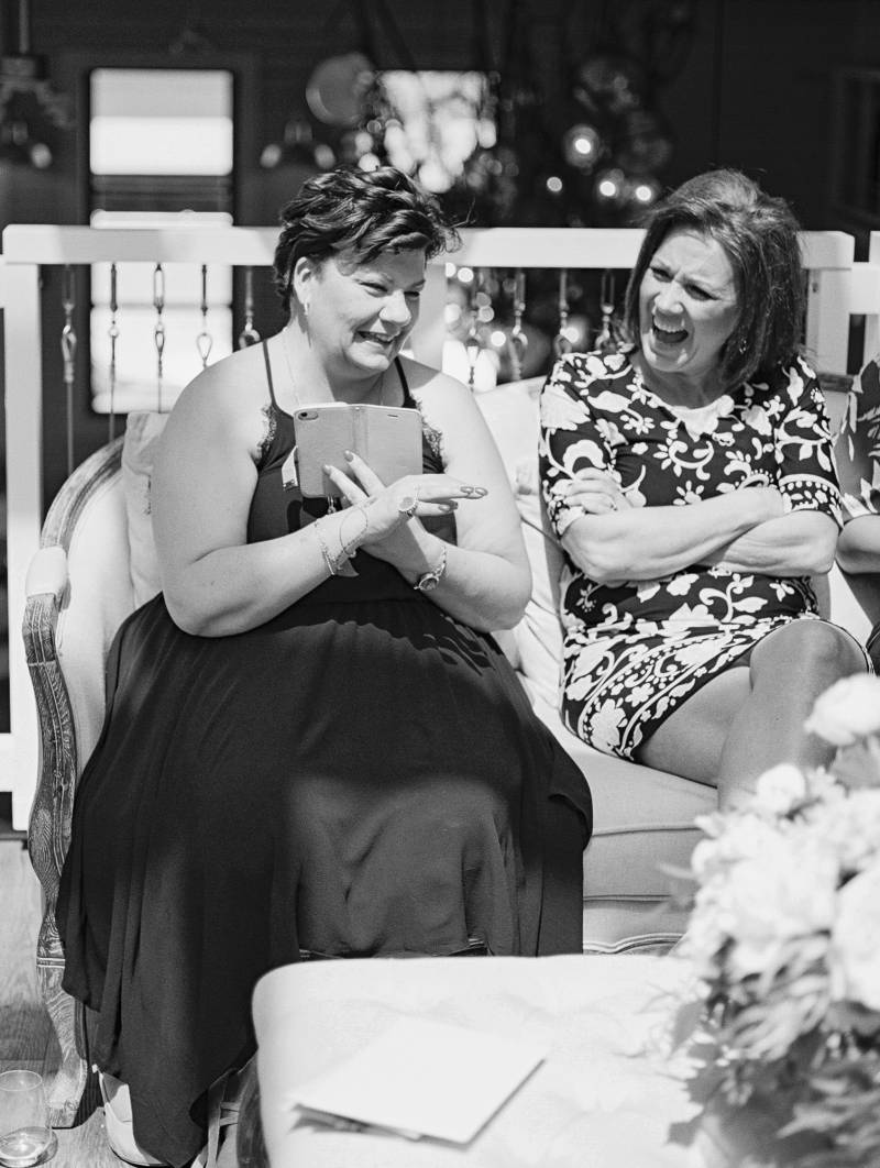 Two women sitting on couch laughing together with their arms crossed 