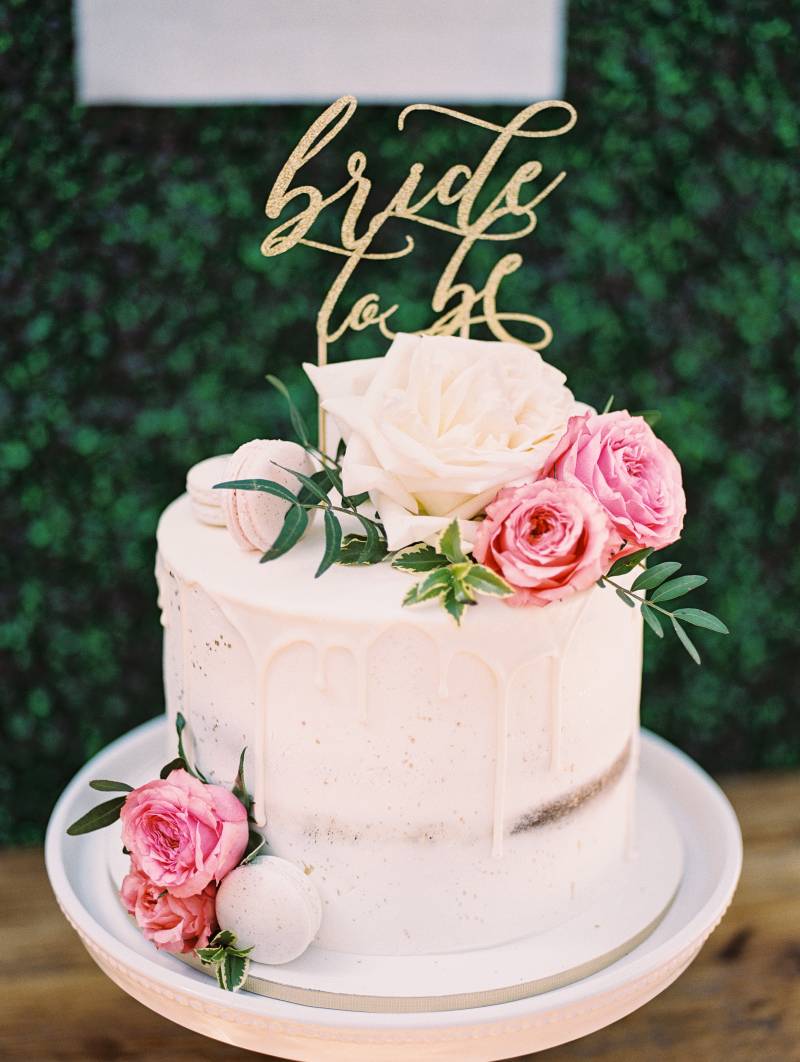 White naked cake with pink and white floral accents and gold lettering 