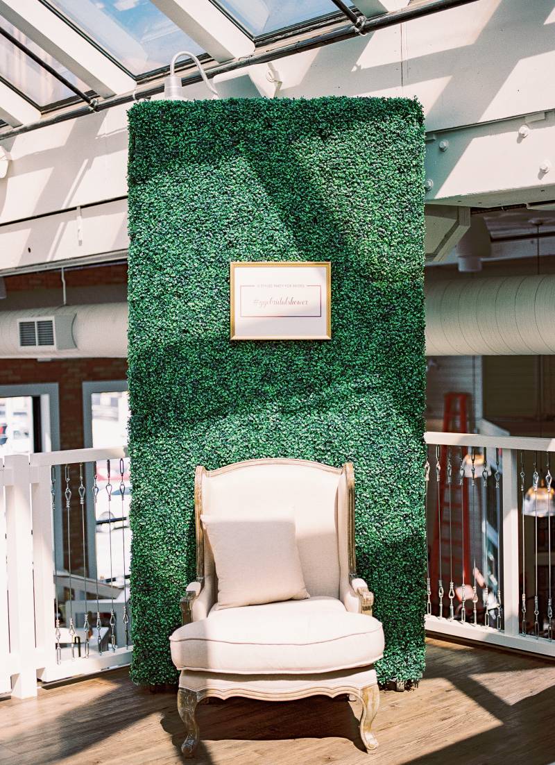Beige and oak seat in front og large greenery wall with pale pink sign