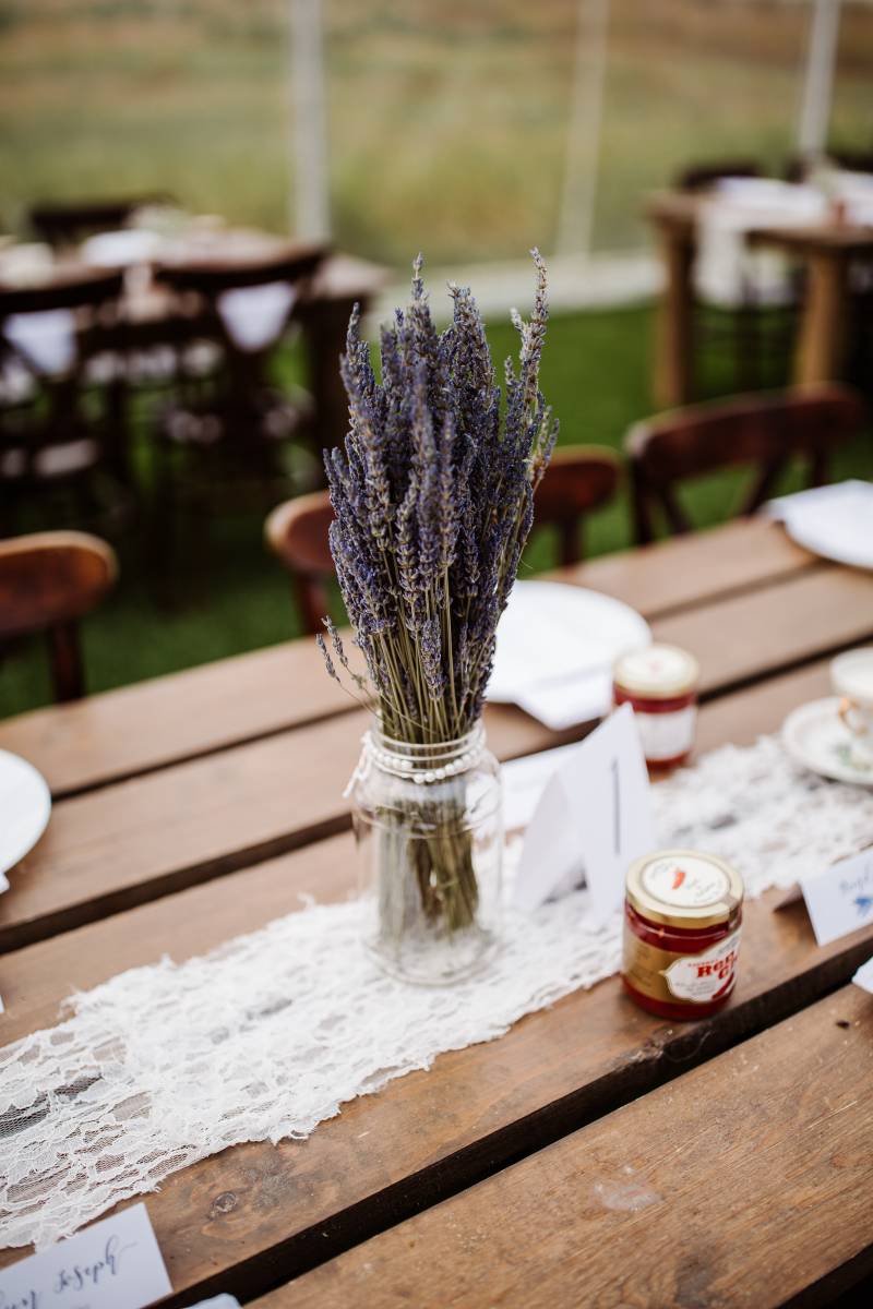 Lavender flowers in mason jar on wooden guest table with white table runner 