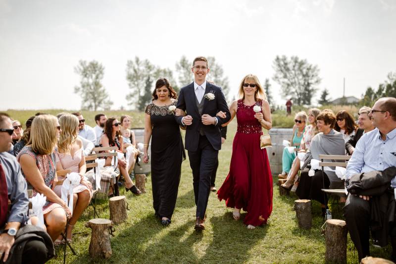 Groom walking the aisle in dark suit in arms with women in black and maroon red dress