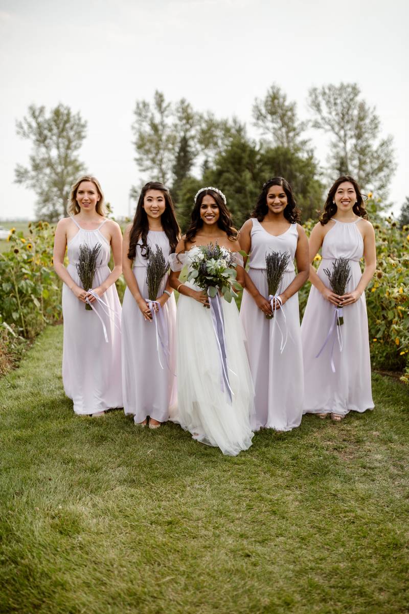 Bride and bridesmaids holding lavender bouquets in sunflower patch