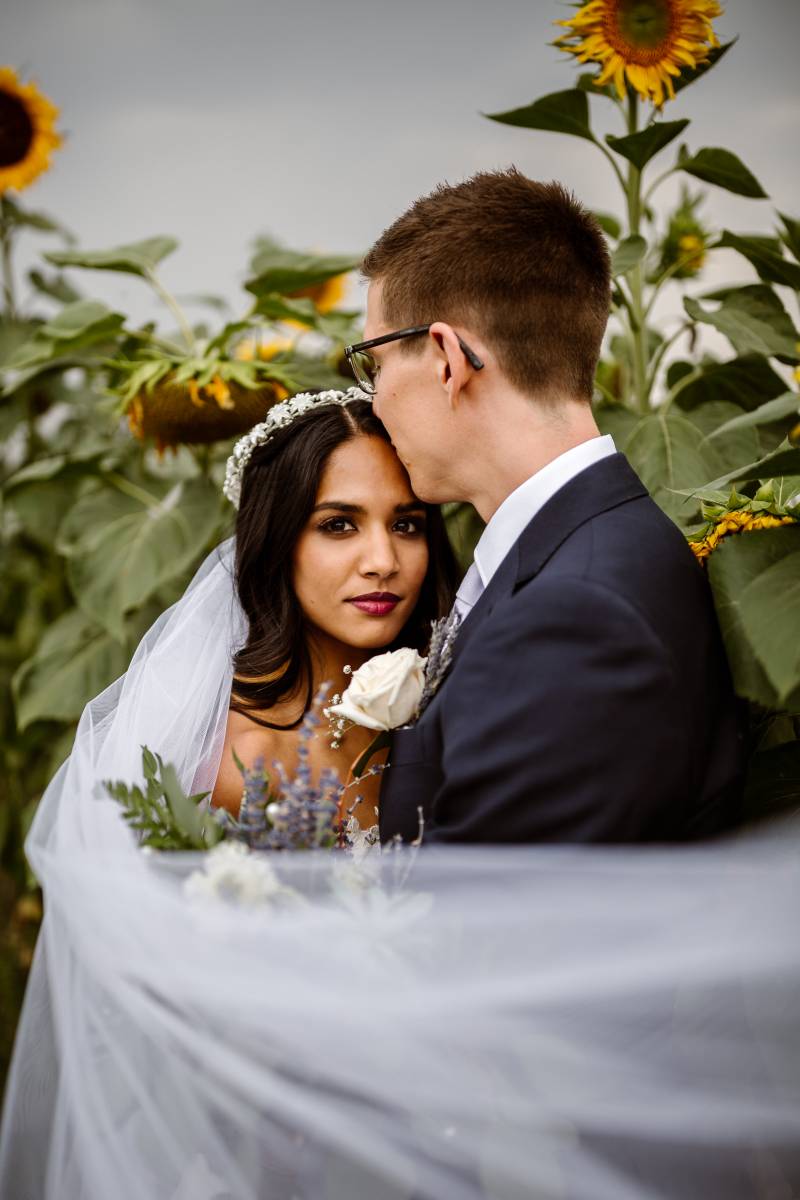 Bride and groom in sunflower patch with lavender bouquet and white flower crown 