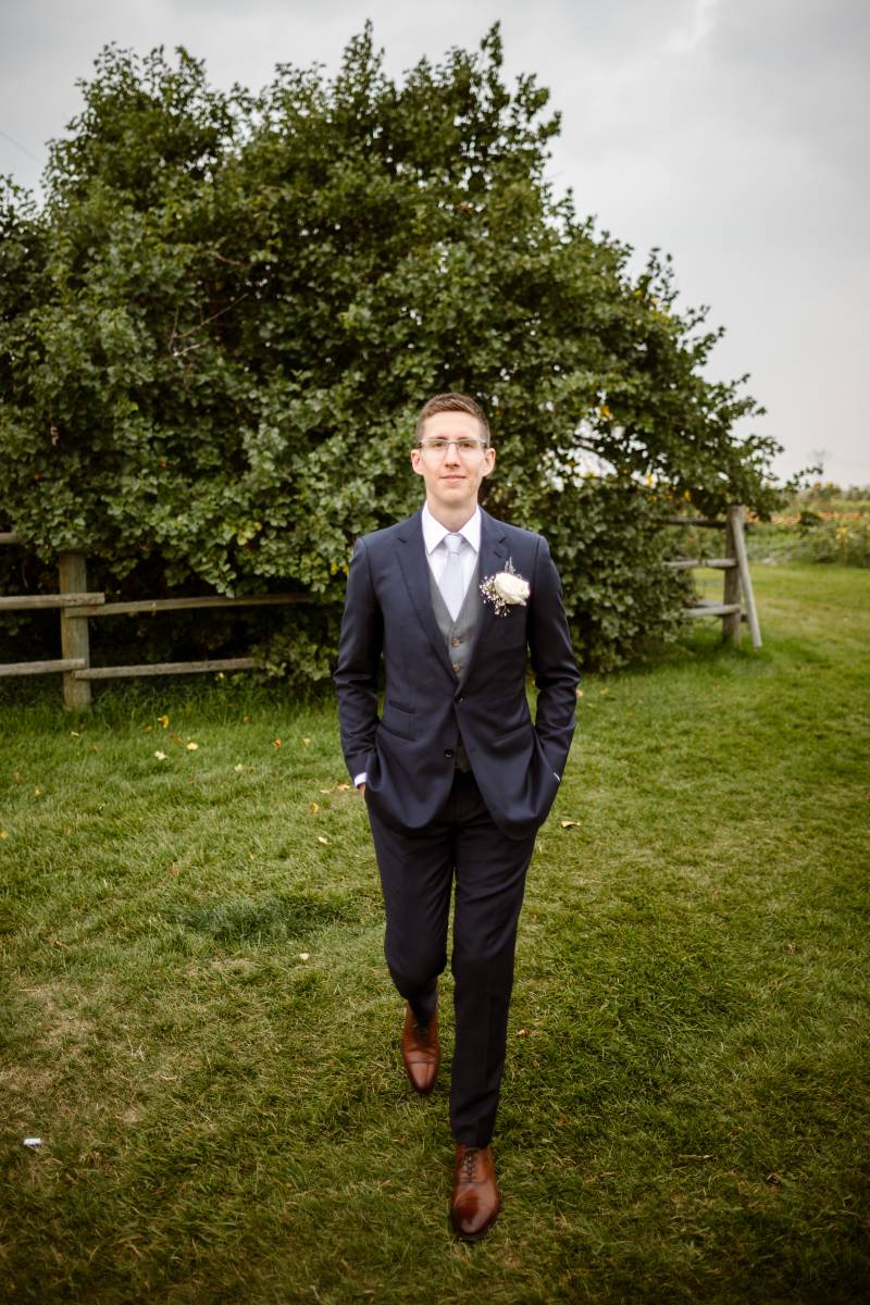 Groom walking towards camera with dark blue suit and lavender tie with brown shoes 