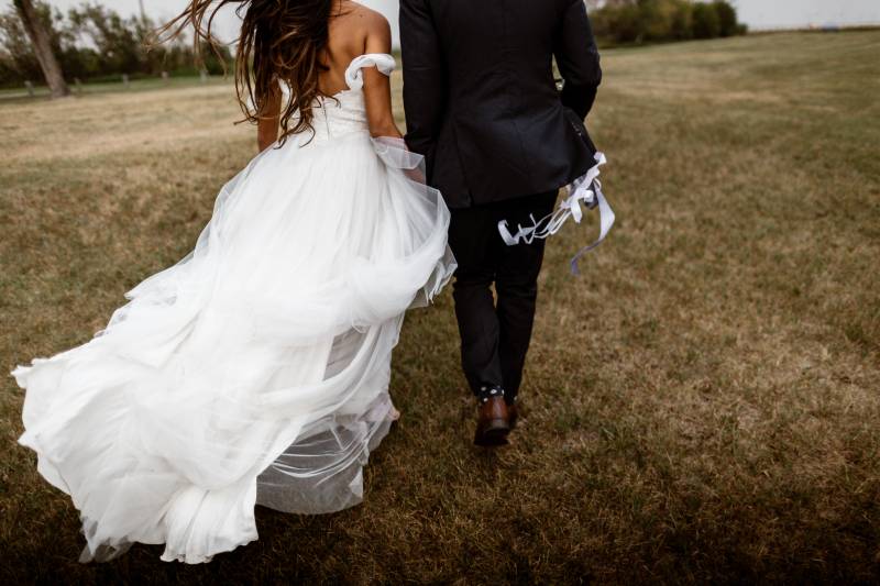 Bride and groom walking together in field with lavender ribbons in the wind