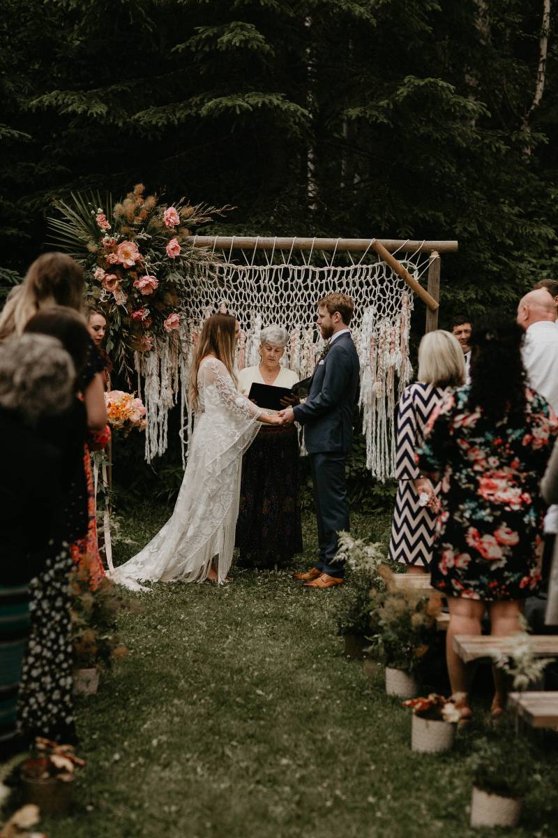 Bride and groom wedding vows in front of macramé wedding arch and blush floral arrangements 