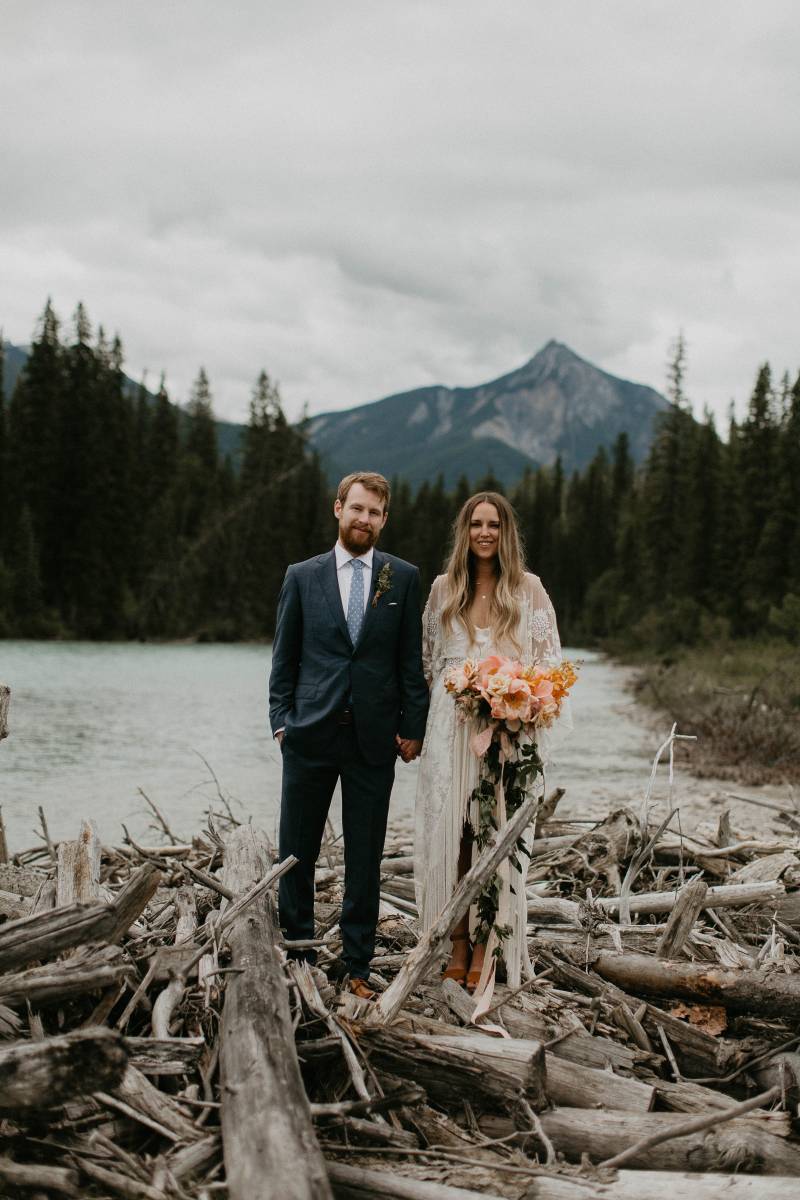 Bride and groom on wooden river dam with mountain background 