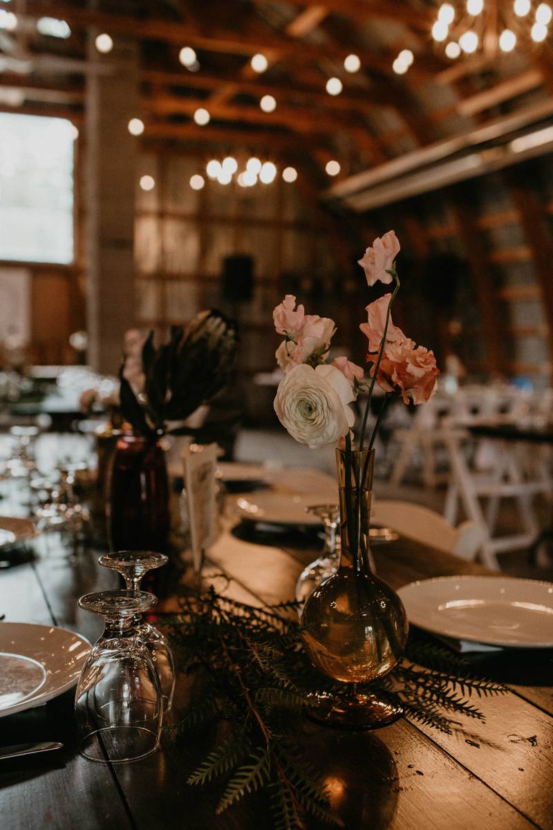 Barn wedding reception with blush flowers in vase on dark wood table 