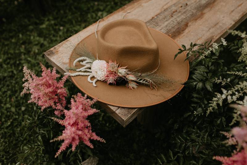 Suede hat with blush fascinator on wooden bench and blush floral accents 