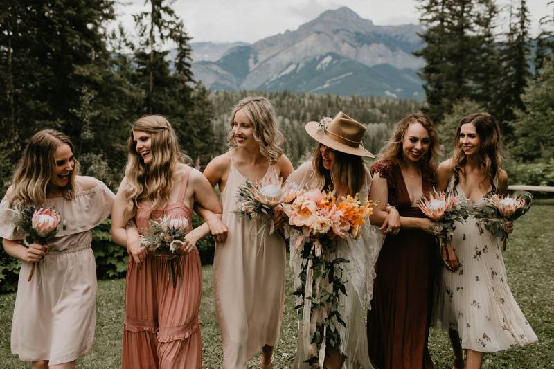 Bridesmaids wearing blush and burgundy dresses linking arms with blush floral bouquets 